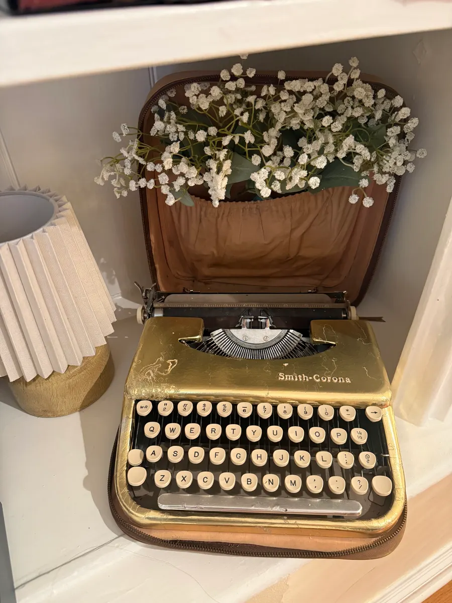 A vintage typewriter on a desk beside a sprig of baby’s breath