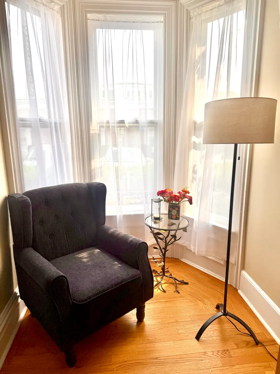 A dark blue armchair beside the bay window, with a floor lamp and flowers